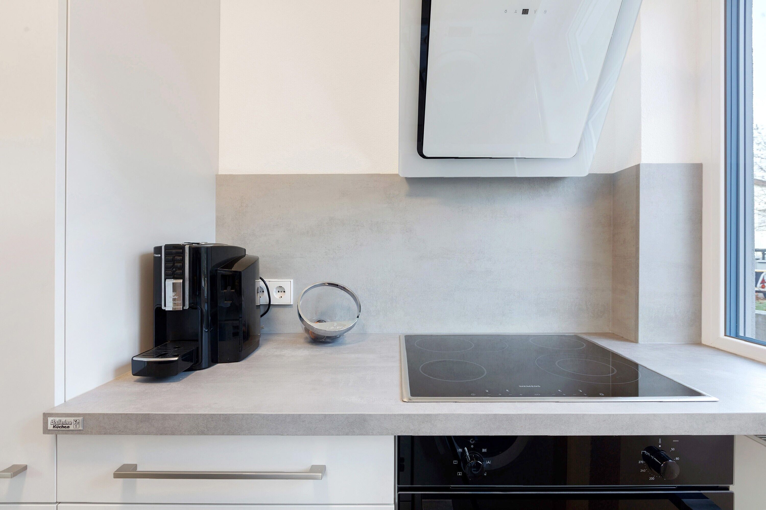 Eine moderne Küche mit integriertem Kaffeeautomat, einer Schüssel und einer schwarzen Induktionskochplatte.