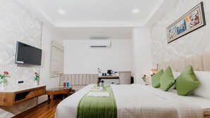 A hotel room with a bed, a desk, a chair, a television, and a painting on the wall. - Emerald Inn (Bhopal)