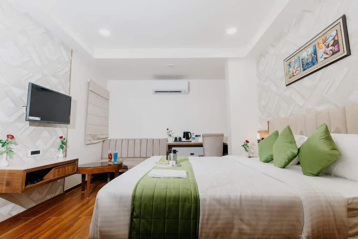 A hotel room with a bed, a desk, a chair, a television, and a painting on the wall.