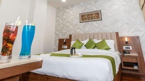 A hotel room with a bed, a nightstand, a bedside table, and a wall with a geometric pattern. - Emerald Inn (Bhopal)