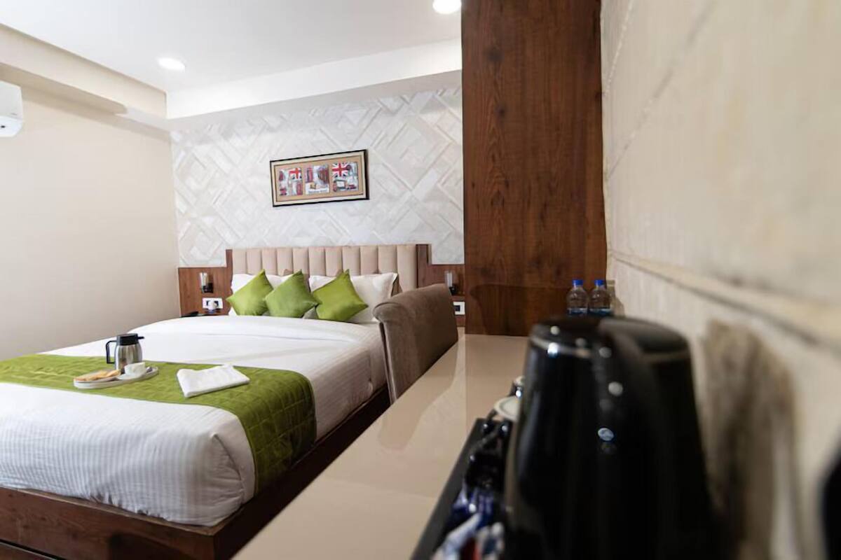 A hotel room with a bed, a wooden headboard, a nightstand, and a coffee maker.