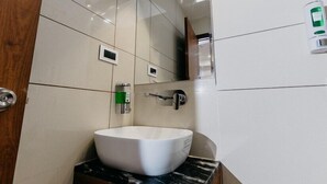 A modern bathroom with a white sink, a mirror, and a soap dispenser. - Emerald Inn (Bhopal)