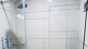 A glass-enclosed shower stall with a handheld showerhead, a glass shelf, and a control panel. - Emerald Inn (Bhopal)