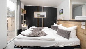 Una habitación de hotel moderna con una cama grande, cabecera de madera, un escritorio pequeño y un ventanal amplio.