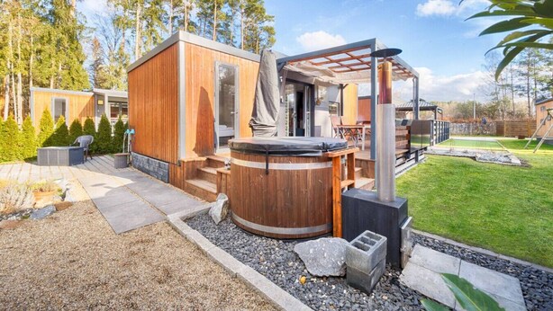 Un área moderna de hidromasaje al aire libre con una terraza de madera, una bañera de hidromasaje y una pérgola.