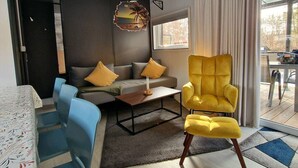 A modern living room with a sofa, a yellow armchair, and a dining area with a table and chairs. - Tiny house on Lake Murner with hot tub (Wackersdorf)