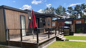 A modern outdoor seating area with a wooden deck, a red umbrella, and a hot tub. - Tiny house on Lake Murner with hot tub (Wackersdorf)