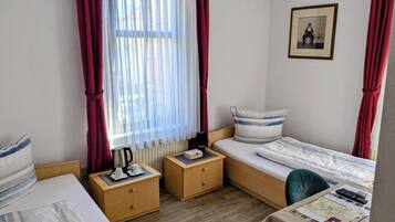 A hotel room with two single beds, a wooden nightstand with a kettle, a table with a map and remote control, and a framed picture on the wall.