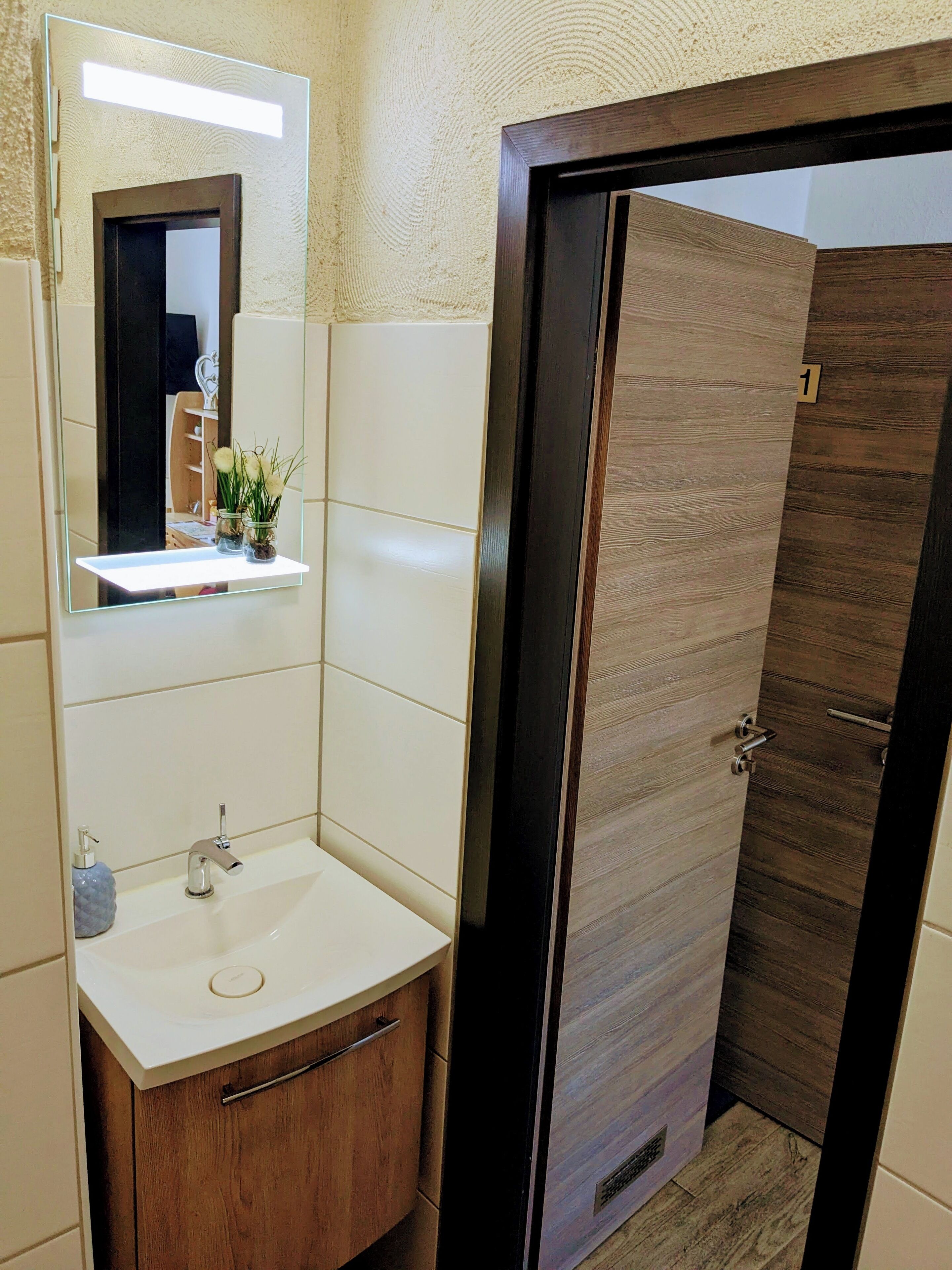 Ein Badezimmer mit einem weißen Waschbecken, einem Spiegel und einer Holztür.