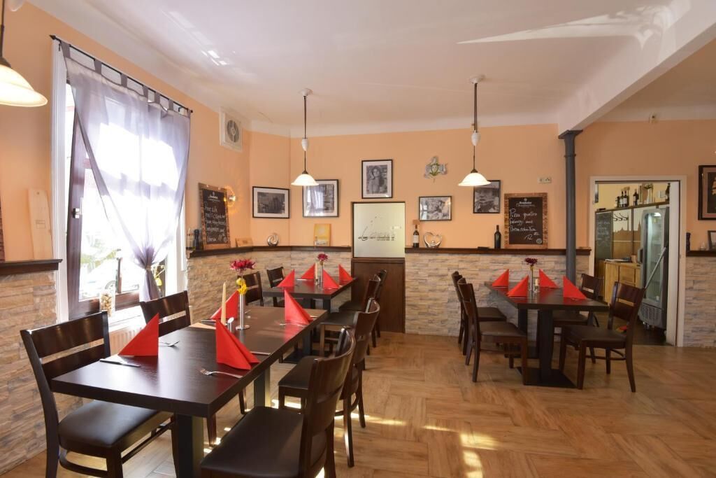 Un restaurante con varias mesas y sillas, piso de madera, iluminación colgante, cuadros en las paredes y un menú en una pizarra.