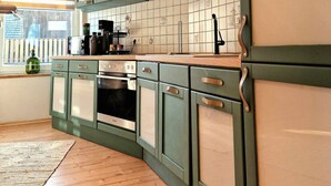 A kitchen with green cabinets, a tiled backsplash, and a window with blinds. - Select-Home 6 - Haus Altstadt (Neunburg vorm Wald)