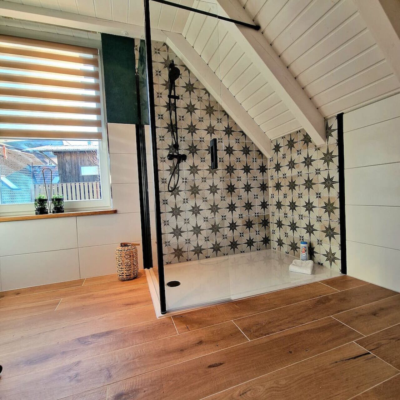 Ein Zimmer mit Holzboden, einem fenster mit Jalousien, einer Dusche mit Sternenmuster an der Wand und einer kleinen Pflanze auf der Fensterbank.