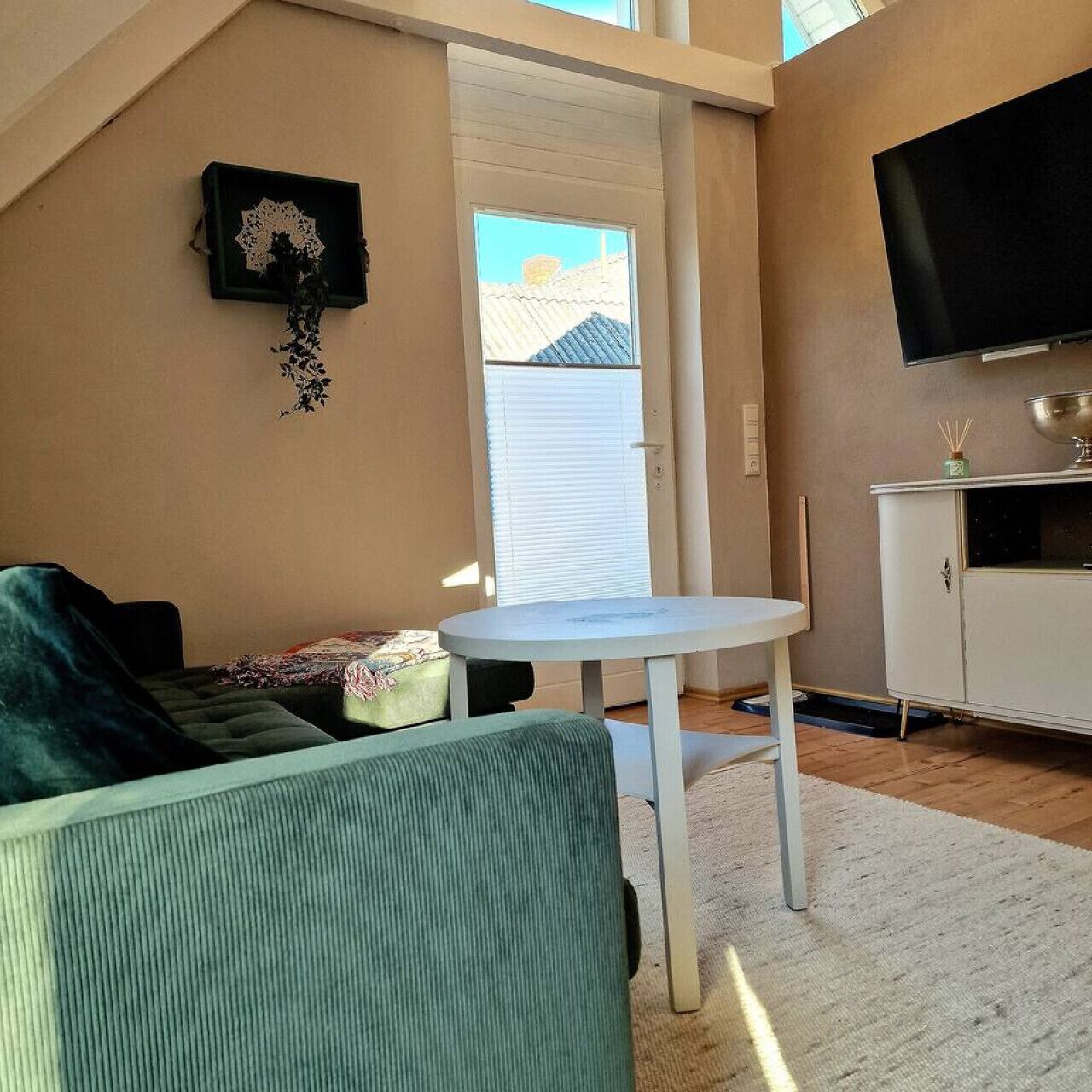 Un salon avec un canapé vert, une table blanche et un téléviseur fixé au mur.