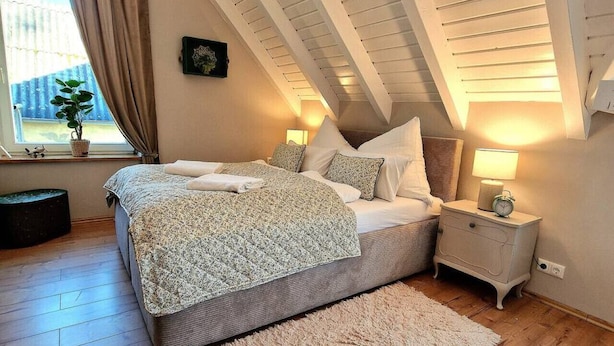 A bedroom with a sloped ceiling, a bed with a patterned bedspread, a nightstand with a lamp, and a window with curtains. - Select-Home 6 - Haus Altstadt (Neunburg vorm Wald)