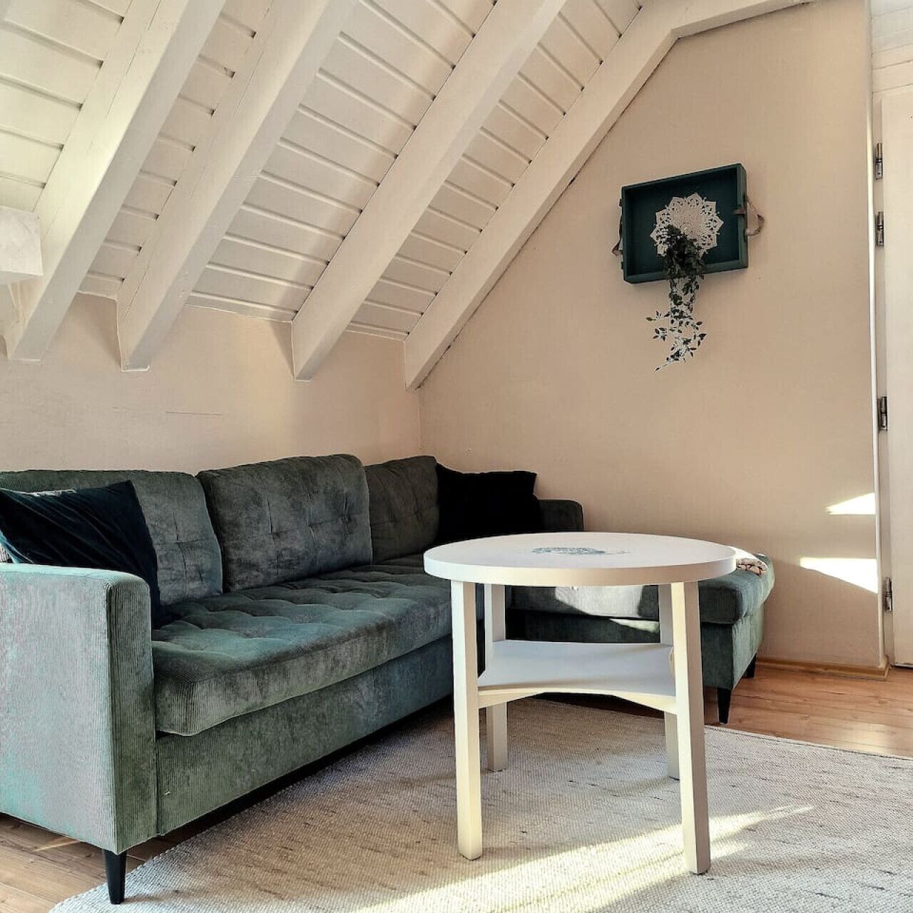 A loft bedroom with a green sofa, a small white table, and a decorative wall piece.