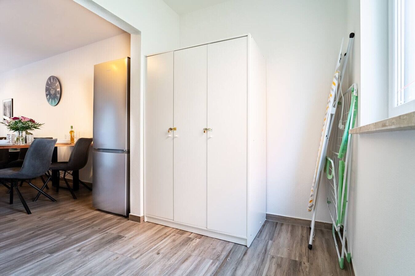 Una habitación moderna con suelo de madera, zona de comedor con mesa y sillas, armario blanco y un radiador en la pared.