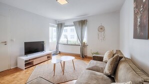 Ein modernes Wohnzimmer mit Flachbildfernseher, einer Couch, einem Couchtisch und einem Fenster mit Vorhängen.