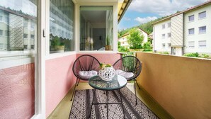 Ein Balkon mit Glastisch, zwei Stühlen und einem Blumentopf.