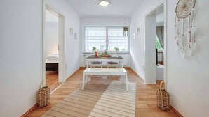 Ein heller Korridor mit einer weißen Bank, einem Tisch mit Pflanzen und einem Traumfänger an der Wand.