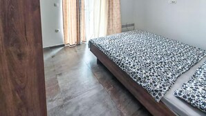 Un dormitorio con cama, suelo de madera, una ventana con cortinas y un termostato en la pared.