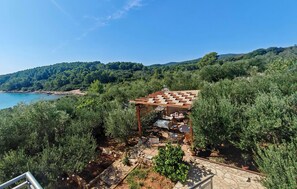 A rustic outdoor seating area with a pergola, surrounded by dense greenery and overlooking a coastal landscape. - Lovely apartment in Lumbarda with house sea view (Lumbarda)