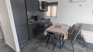 Una cocina compacta con armarios oscuros, una pequeña mesa de comedor con sillas y una ventana con persianas.