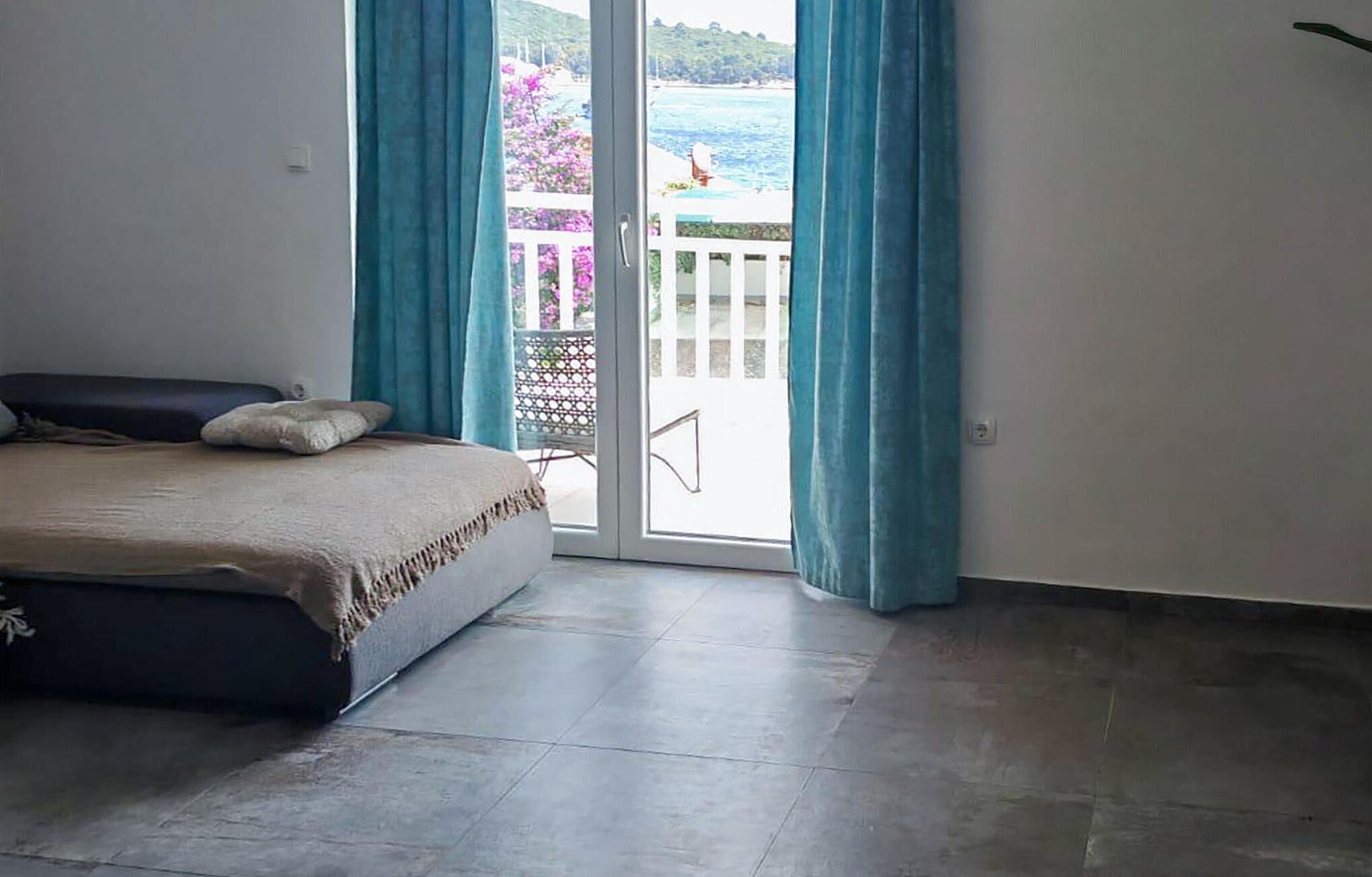 Une chambre avec un lit, une vue sur la mer par une porte coulissante et un balcon doté d’une balustrade blanche.