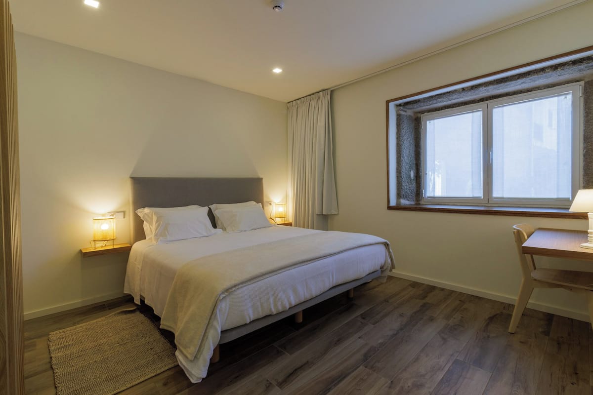 Een slaapkamer met een bed, nachtlampjes, een bureau en een raam.