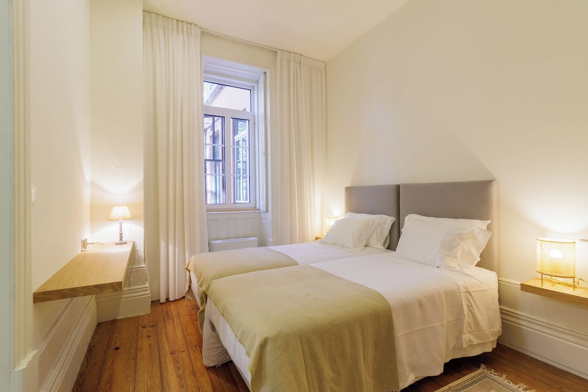 Een slaapkamer met twee bedden, een raam met gordijnen, bedlampjes en een houten vloer.
