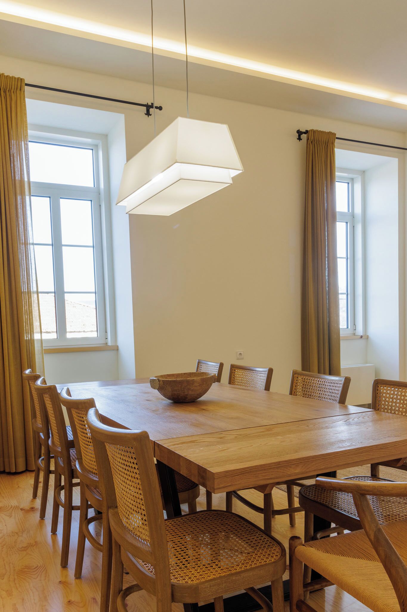 Un comedor con una mesa de madera, seis sillas de mimbre, un tazón grande y una lámpara colgante.