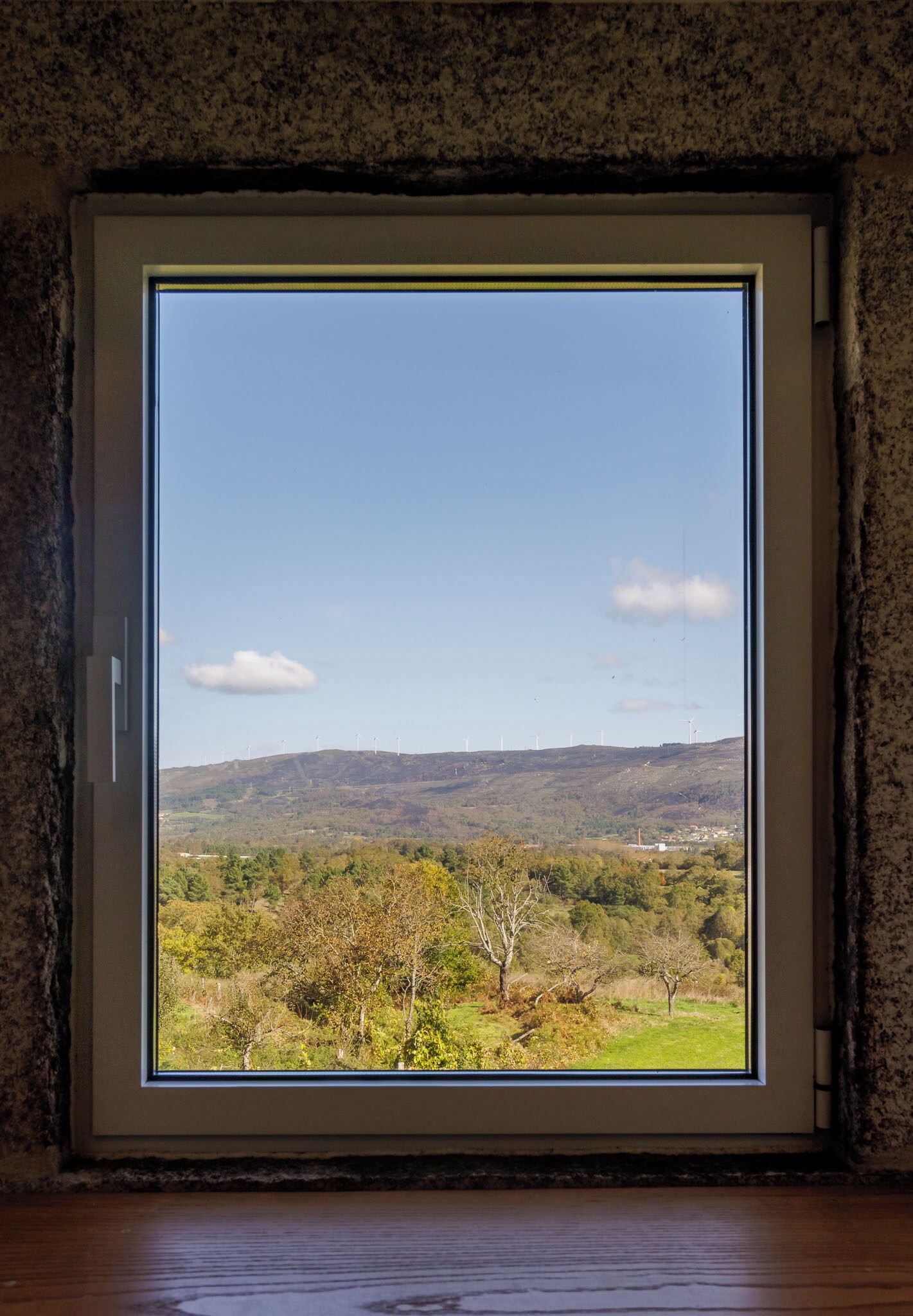 A room with a large window offering a view of a hilly landscape with trees and wind turbines.