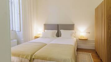 A double room with two beds, each with a bedside table and lamp, a wooden wardrobe, and a window with curtains.
