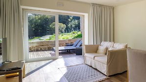 Een woonkamer met een bank, een salontafel en een televisie op een houten dressoir. Er is een schuifdeur naar een buitenruimte met een tuin en een stenen muur.