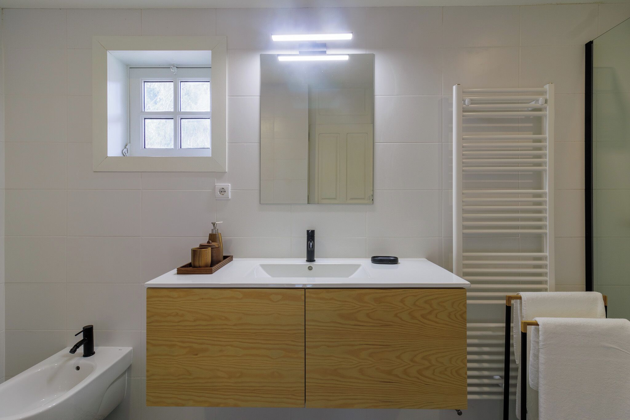 A modern bathroom with a white sink, wooden vanity, a mirror, a towel rack, and a towel hanging on it.