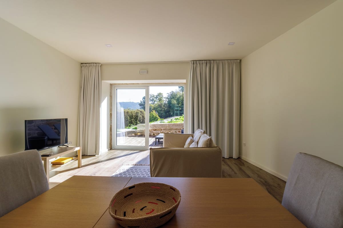 Een woonkamer met een televisie, een tafel en uitzicht op de omgeving.