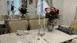 Un comedor con una gran mesa blanca, varias sillas, una araña y un tablero de ajedrez.