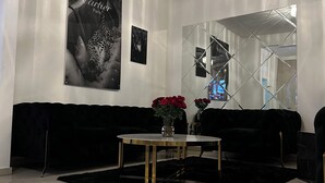 Una sala de estar moderna con un sofá negro, una mesa redonda de centro con flores rojas y una lámpara de araña.