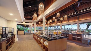 Amplia zona de buffet con una isla central, paneles de madera y lámparas colgantes.
