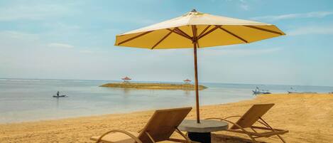 A beach with two wicker lounge chairs and a large umbrella.