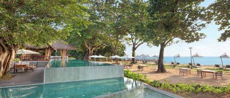 A pool area with a clear view of the sea, surrounded by trees and outdoor seating.