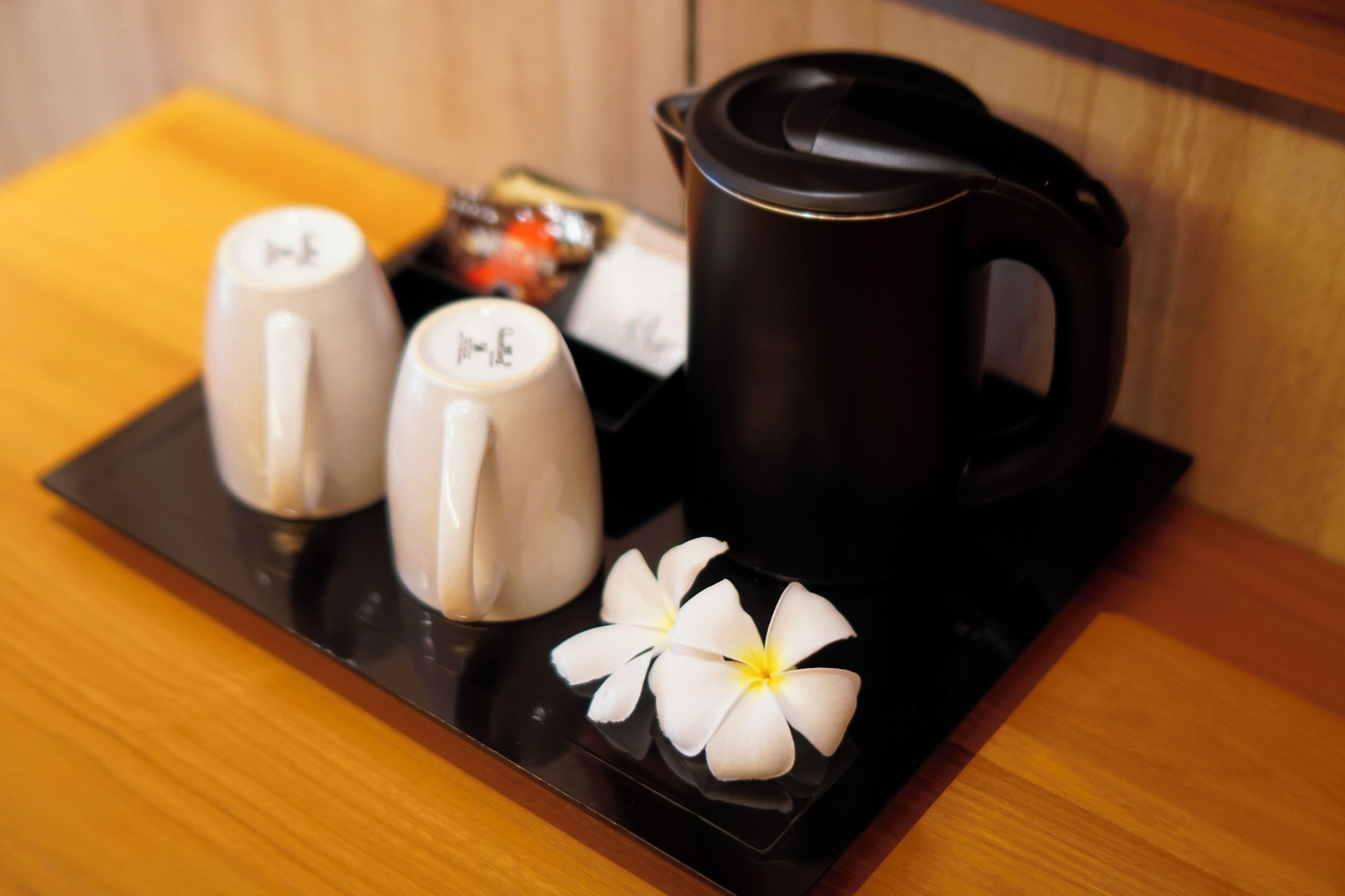 A tray with a black coffee pot, two white ceramic cups, and two white flowers on a wooden surface.
