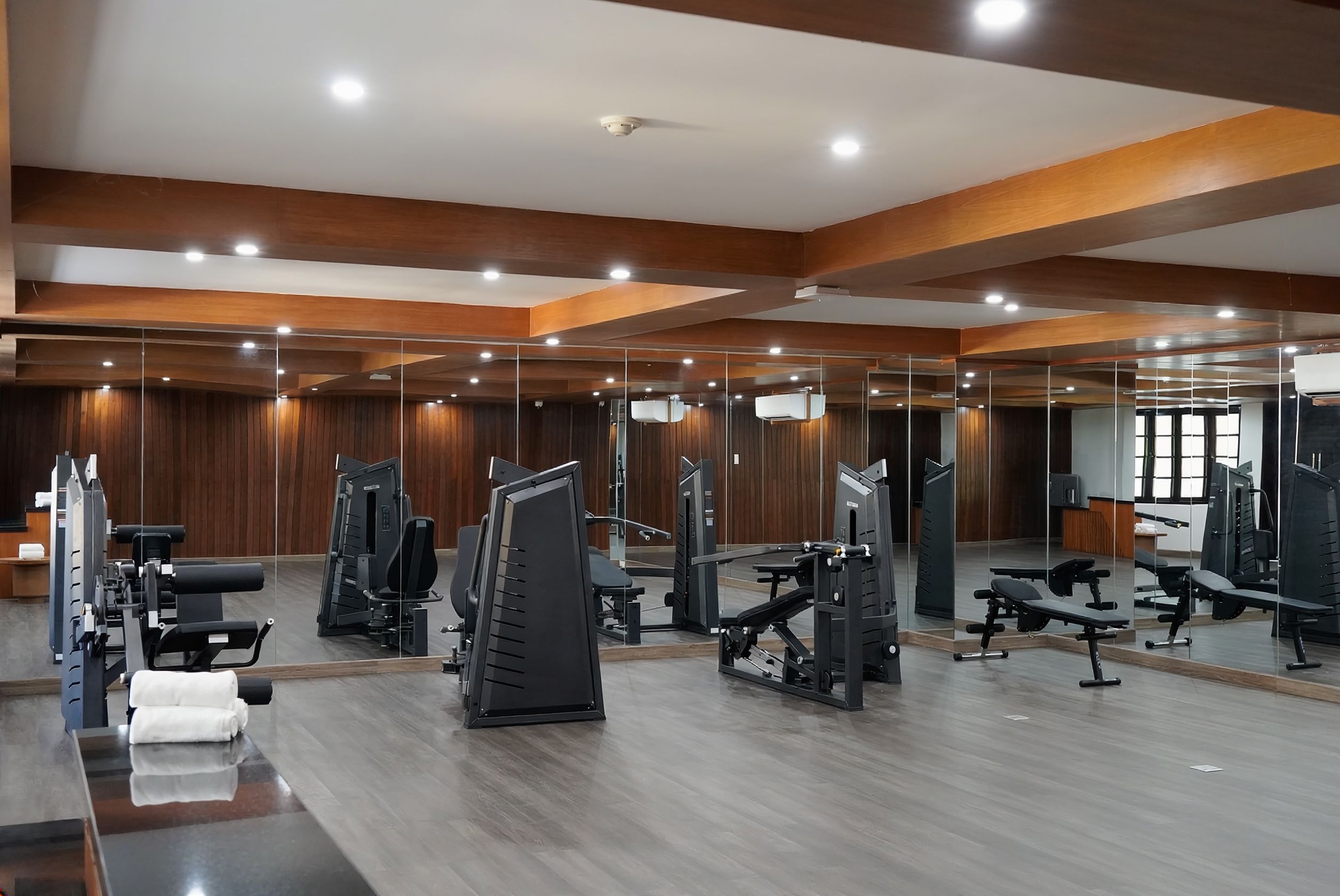 A gym with various exercise equipment, wooden floors, and a large mirror wall.
