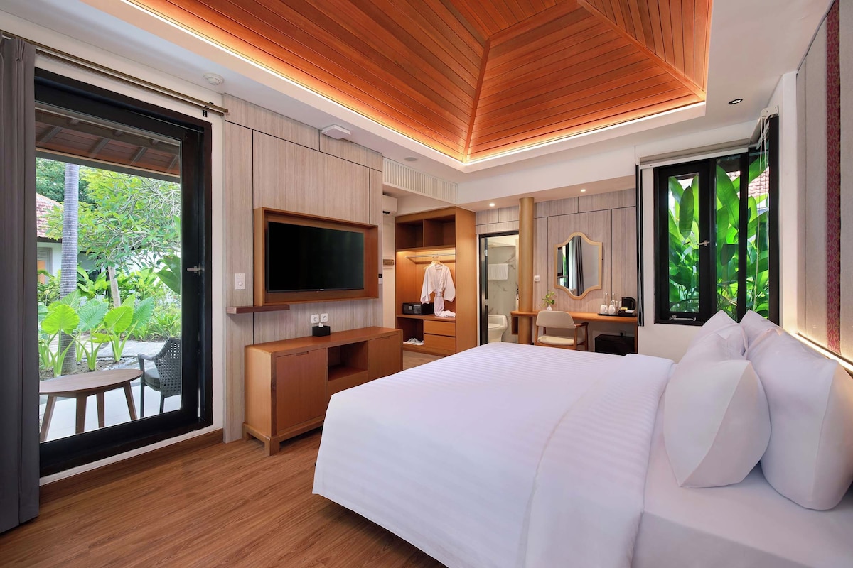 A modern hotel room with a large bed, wooden ceiling, a TV, a desk, and a bathroom with a mirror.