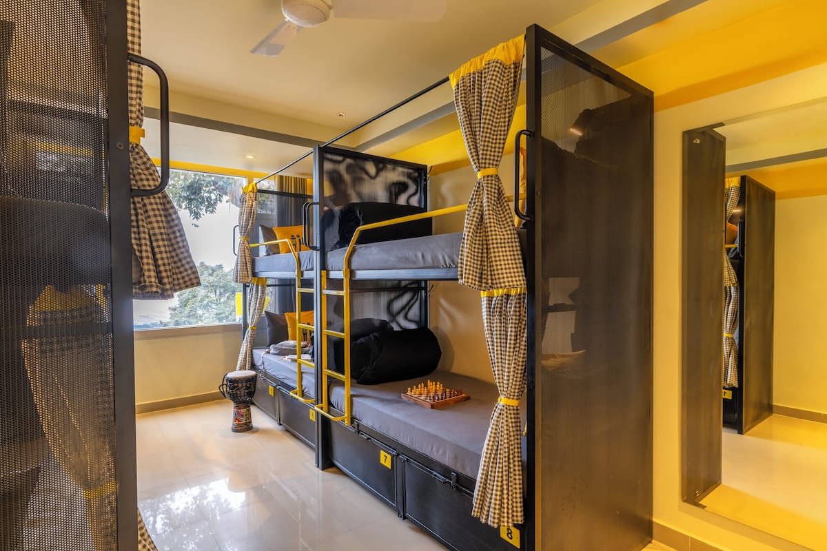 A bunk bed room with a chessboard on the lower bunk, a ladder, and a window with a view of trees.