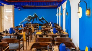 Un restaurante con paredes azules y mesas de madera, que presenta un mural de montañas en la pared de fondo.