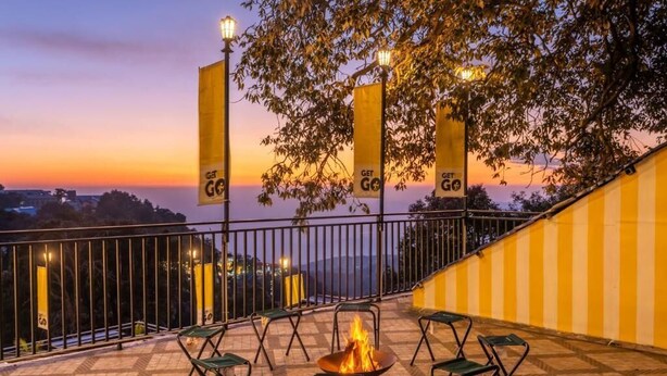 Una terraza exterior con un brasero, sillas y vistas al atardecer.