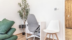 A room with a grey office chair, a white chair, a green sofa, and a potted plant. - Lovely Apartment Steps from Schonbrunn (Vienna)