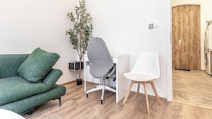 A modern living room with a green sofa, a grey office chair, a white chair, and a wooden door in the background. - Lovely Apartment Steps from Schonbrunn (Vienna)