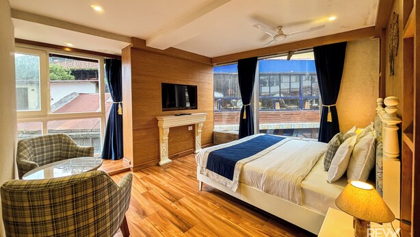 A hotel room with a bed, a TV, a fireplace, a chair, and a window with curtains. - Hotel Park Wood - Mall Road  (Mussoorie)