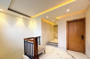 Un intérieur moderne avec une porte en bois portant le numéro « 202 », un escalier en marbre et un garde-corps agrémenté d’un banc.